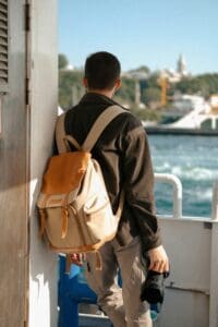 A guy with a backpack and camera looking out into the ocean from a ship