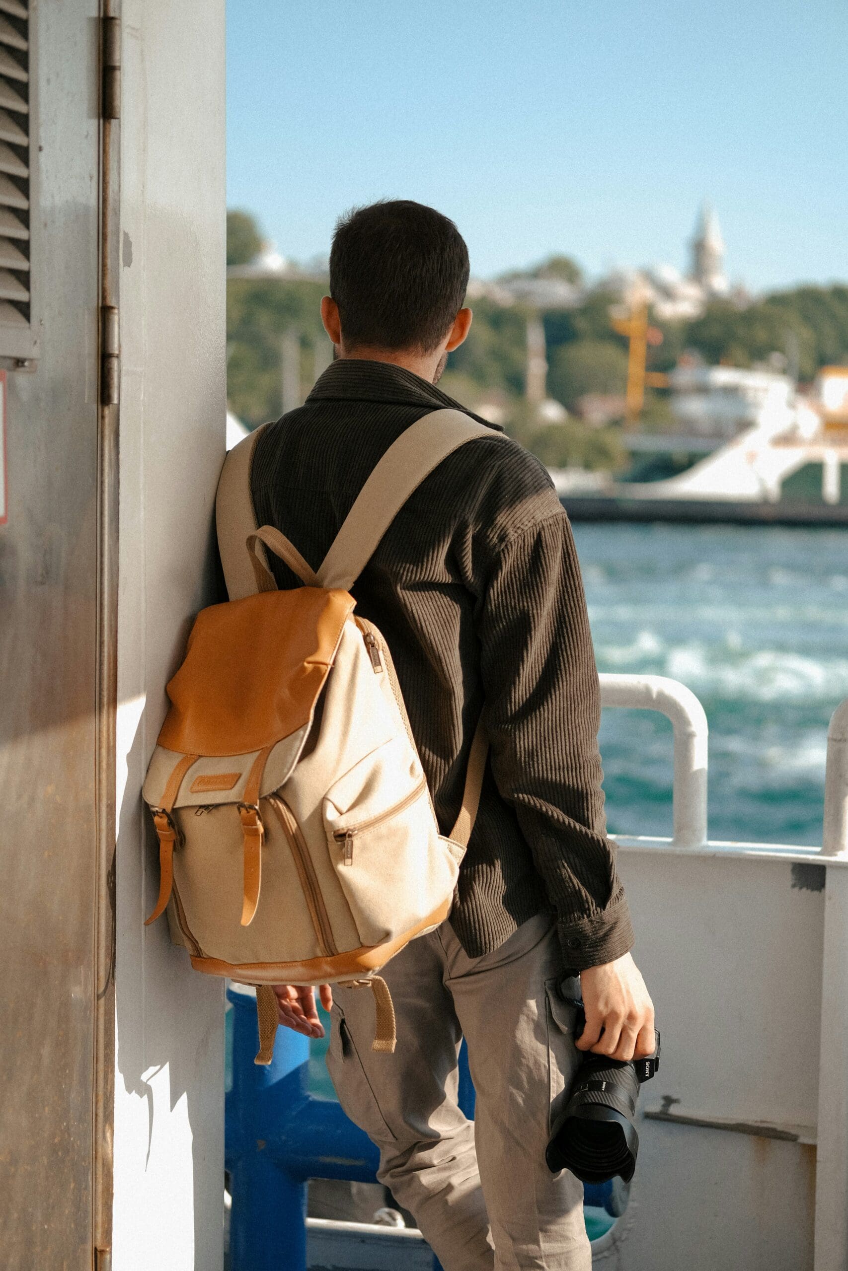 A guy with a backpack and camera looking out into the ocean from a ship