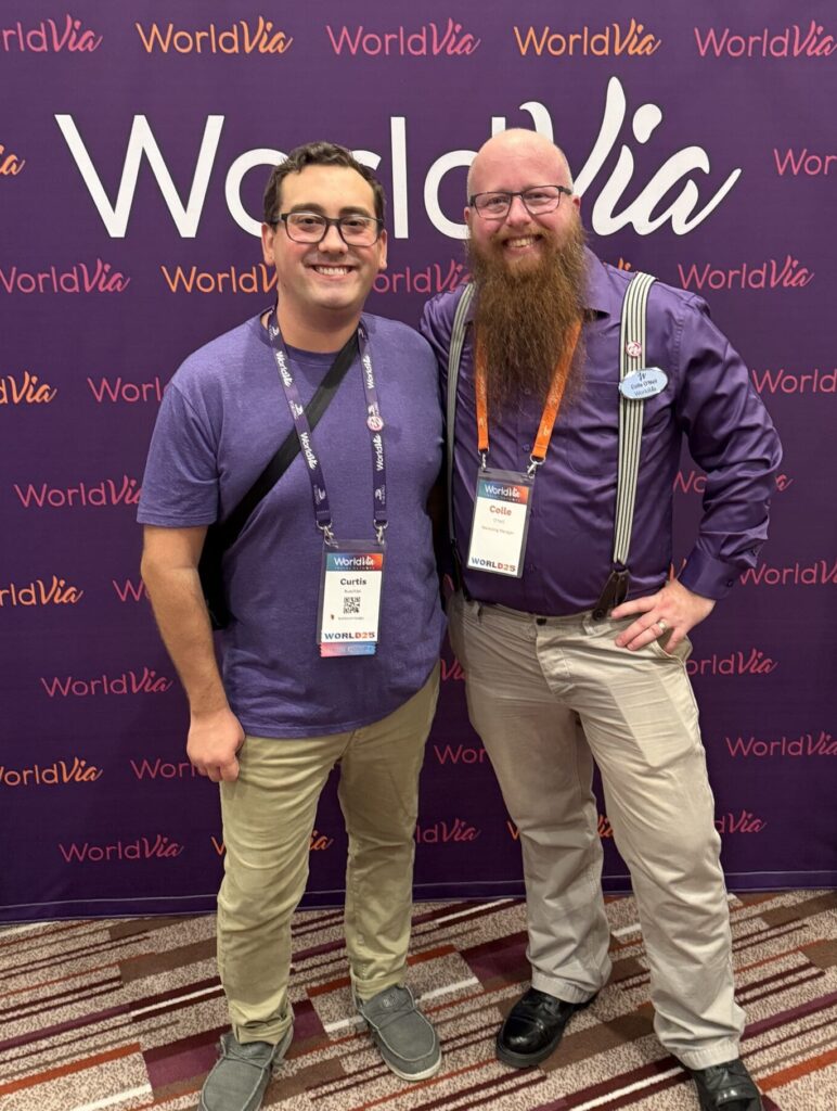 Curtis Buechler and Colle O'neil standing in front of a WorldVia backdrop for the Purple Party at WORLD25.